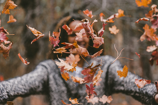 Woman throwing fall leaves | Fall bucket list 10 impactful fall activities