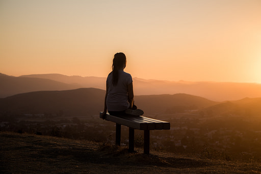 Woman sitting on bench facing orange sunset | Fall bucket list 10 impactful fall activities