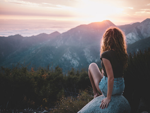 Woman sitting on rock facing sunset | Fall bucket list 10 impactful fall activities
