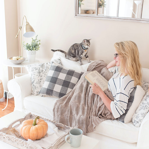 Woman reading on couch with cat and blanket | Fall bucket list 10 impactful fall activities