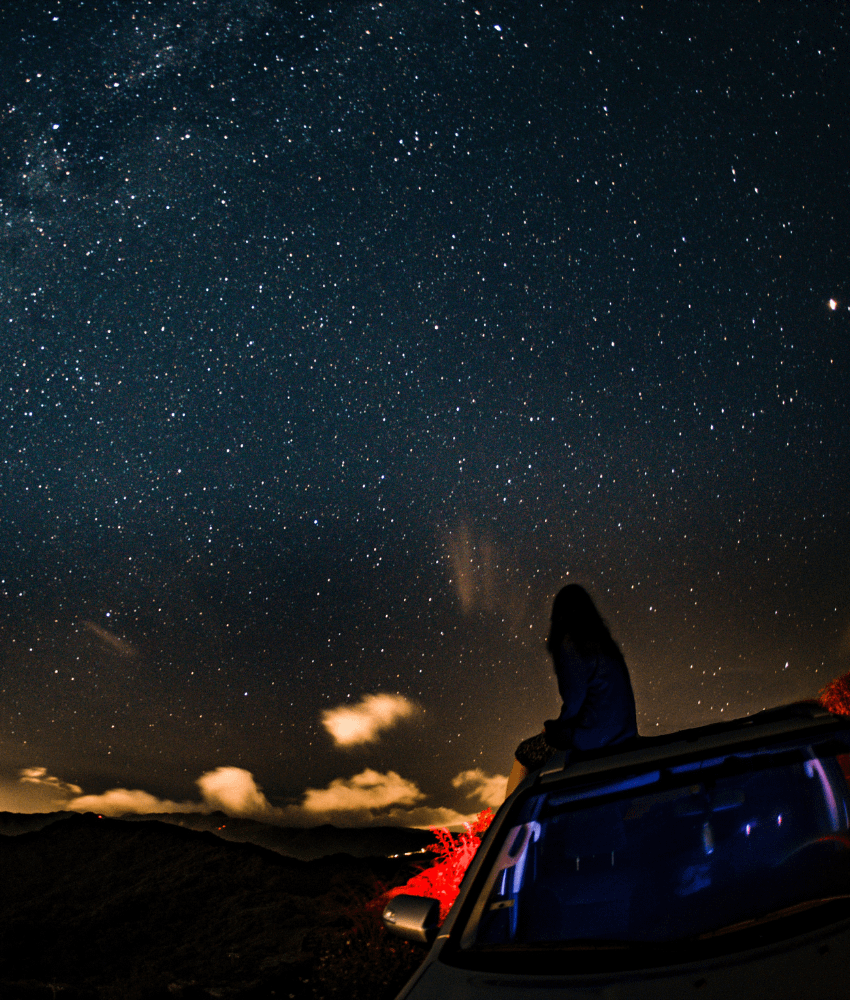 Woman sitting on the roof of the van and stargazing