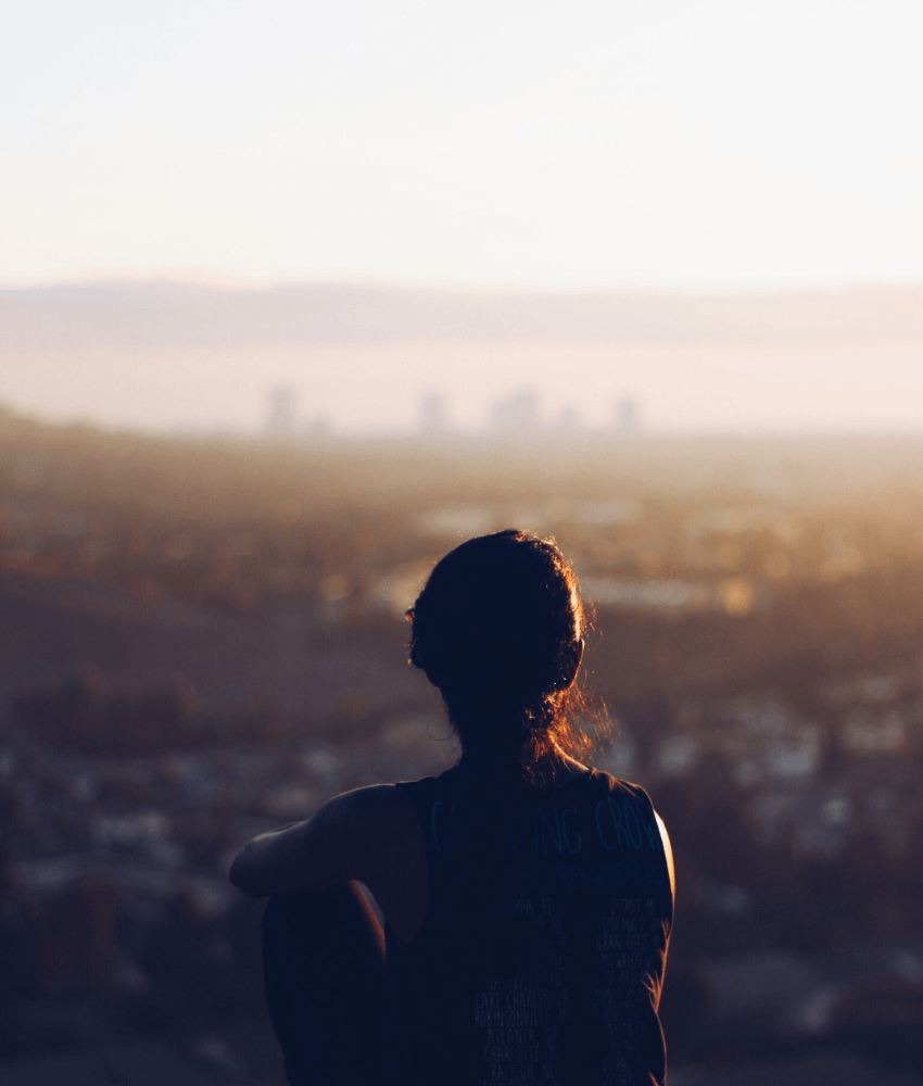 Woman sitting on top of the hill and overlooking the city skyline