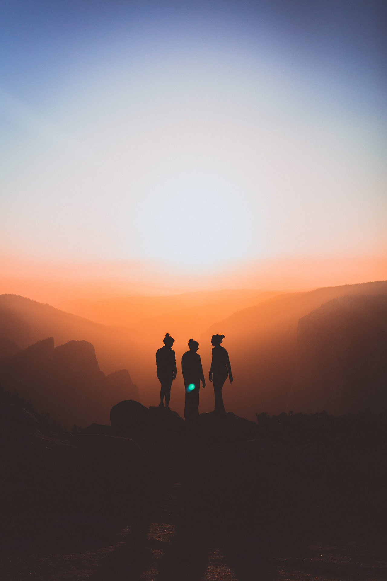 Three women at the mountain summit at sunset